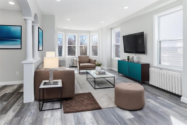 living area with radiator heating unit, wood finished floors, and ornate columns