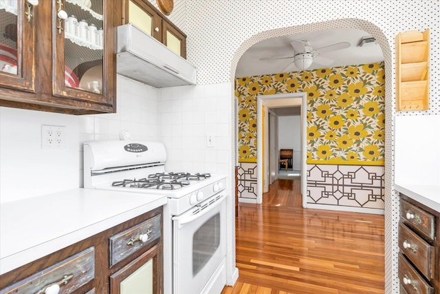 kitchen with white gas range, wallpapered walls, under cabinet range hood, and a ceiling fan