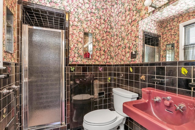 full bathroom featuring wallpapered walls, tile walls, a shower stall, and a sink