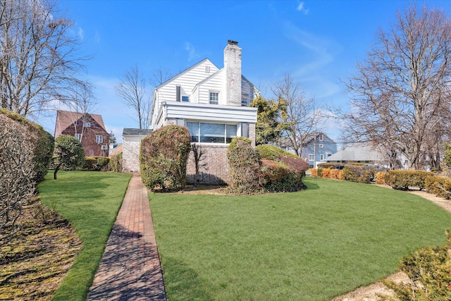 view of side of property with a yard, brick siding, and a chimney