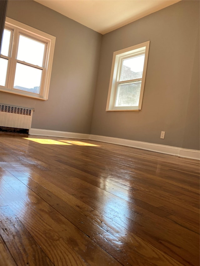 unfurnished room featuring dark wood finished floors, radiator heating unit, and baseboards