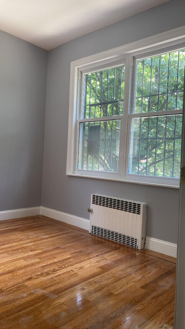 unfurnished room featuring radiator heating unit, wood finished floors, and baseboards