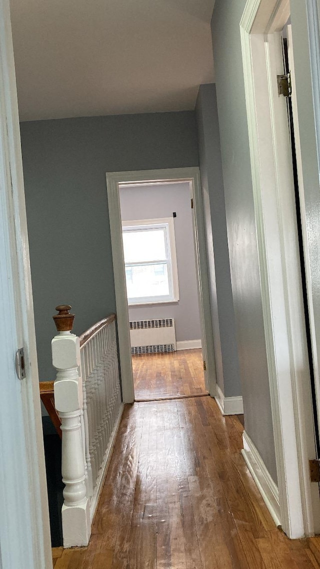 corridor featuring radiator heating unit, baseboards, and hardwood / wood-style floors