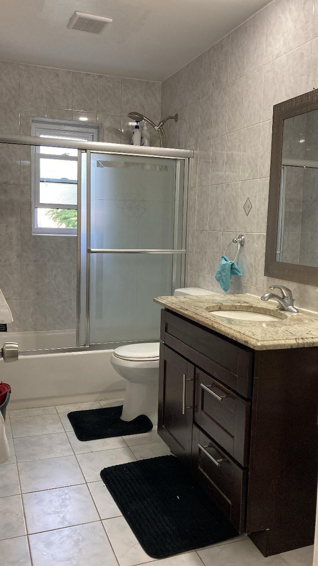 bathroom featuring visible vents, toilet, shower / bath combination with glass door, tile walls, and vanity