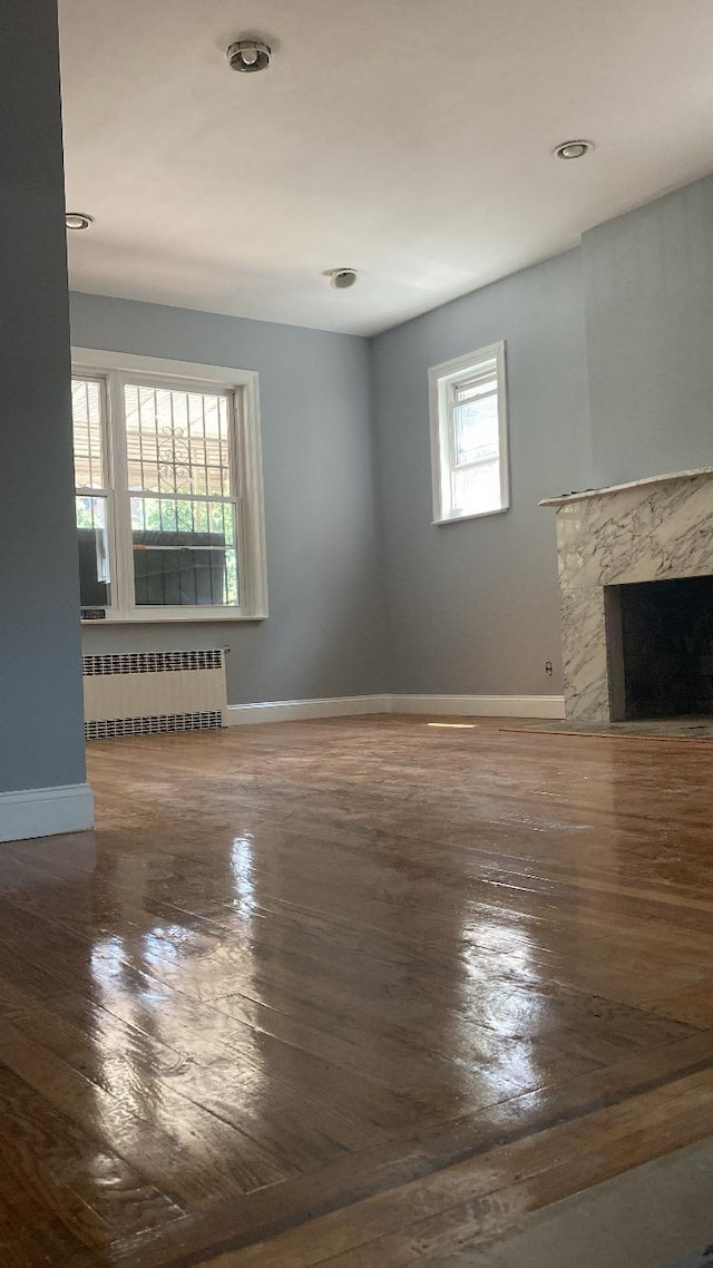 unfurnished living room featuring wood finished floors, radiator heating unit, a fireplace, and baseboards