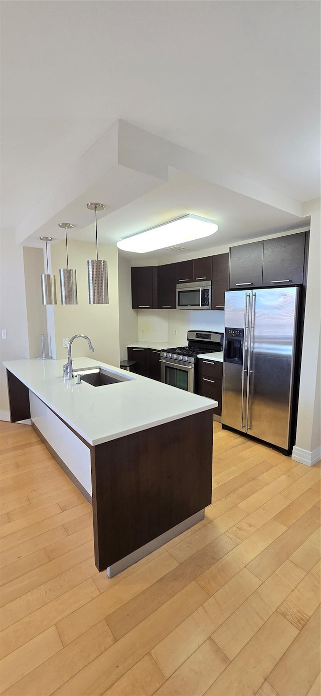 kitchen with light wood-type flooring, modern cabinets, a sink, appliances with stainless steel finishes, and light countertops