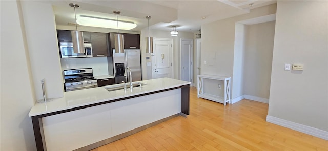 kitchen with light countertops, appliances with stainless steel finishes, a peninsula, light wood-style floors, and a sink