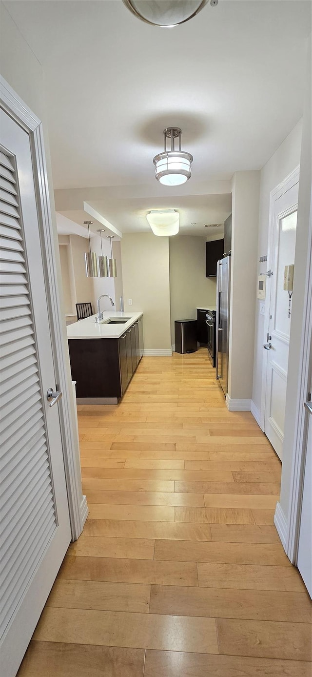 corridor featuring a sink, baseboards, and light wood-style floors