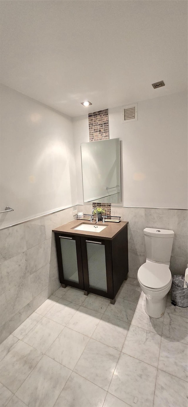 half bath with visible vents, tile walls, and a wainscoted wall