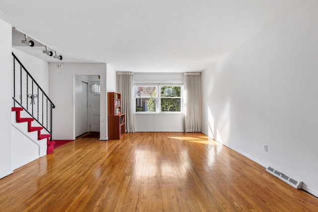 unfurnished living room with stairs, track lighting, visible vents, and wood-type flooring