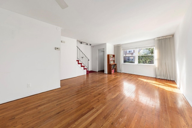 unfurnished living room featuring stairway, a ceiling fan, and wood-type flooring