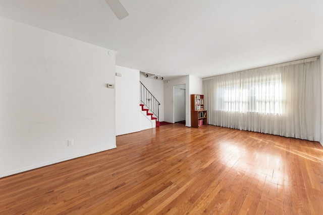 unfurnished living room with stairway, ceiling fan, and hardwood / wood-style floors