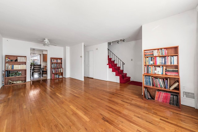 living area featuring stairway, wood-type flooring, visible vents, and ceiling fan with notable chandelier