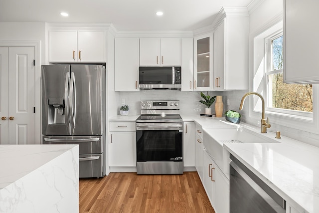 kitchen featuring light stone counters, decorative backsplash, light wood-style flooring, white cabinets, and stainless steel appliances