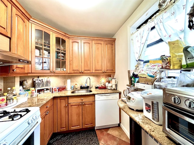 kitchen with white appliances, decorative backsplash, light stone counters, glass insert cabinets, and a sink