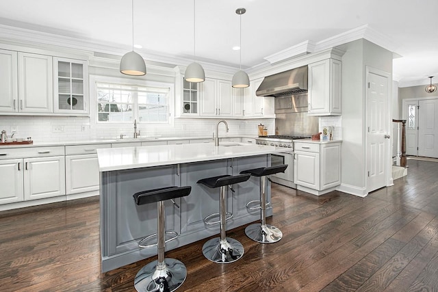 kitchen featuring a sink, stainless steel range, glass insert cabinets, a kitchen breakfast bar, and wall chimney exhaust hood