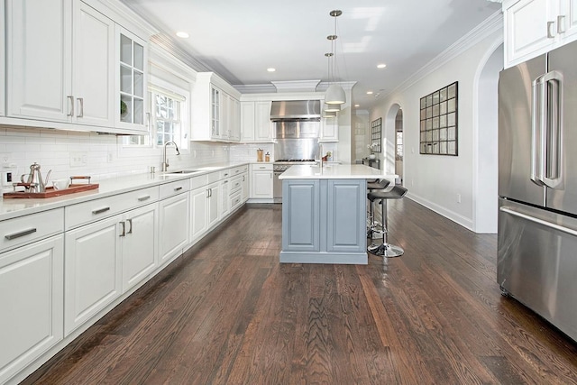 kitchen featuring wall chimney range hood, ornamental molding, appliances with stainless steel finishes, arched walkways, and a sink