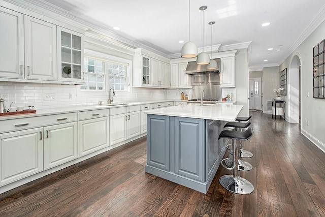 kitchen featuring ornamental molding, a sink, light countertops, white cabinetry, and wall chimney exhaust hood