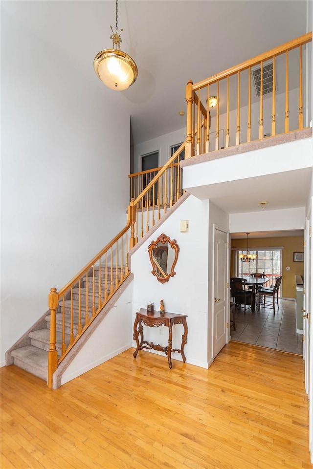 staircase featuring wood finished floors, visible vents, a towering ceiling, and baseboards