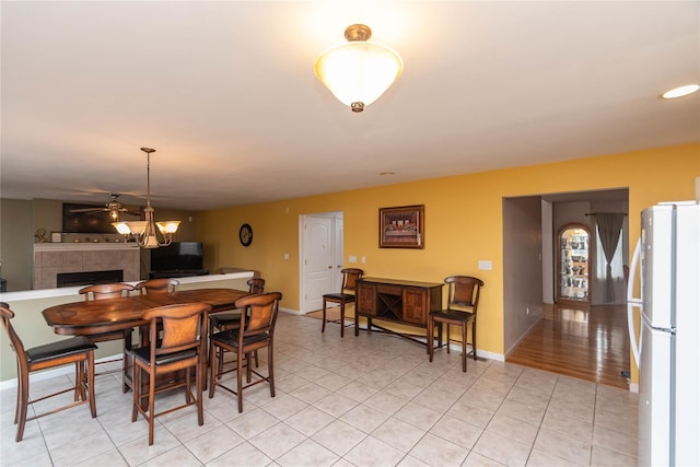 dining room featuring a tiled fireplace, light tile patterned floors, a ceiling fan, and baseboards