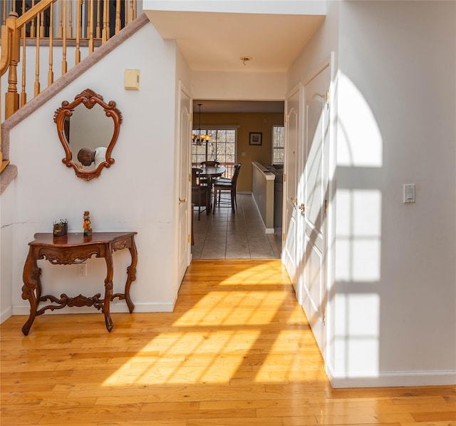 hallway with stairs, light wood-style flooring, a notable chandelier, and baseboards