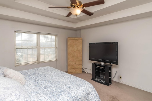 carpeted bedroom featuring baseboards, a tray ceiling, and a ceiling fan