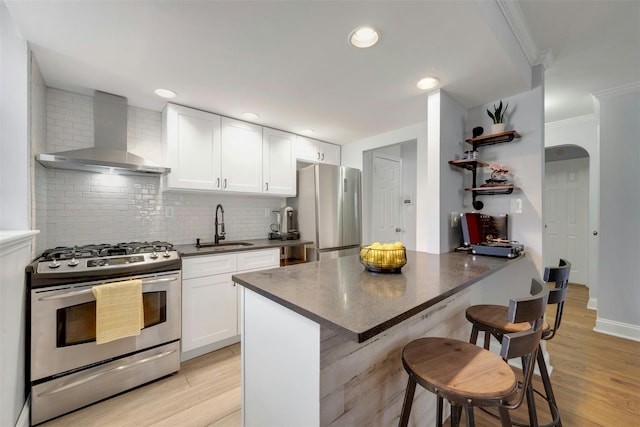 kitchen featuring dark countertops, wall chimney range hood, a kitchen bar, stainless steel appliances, and a sink