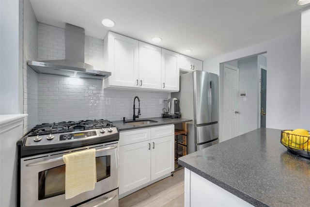 kitchen featuring a sink, stainless steel appliances, white cabinets, dark countertops, and wall chimney range hood