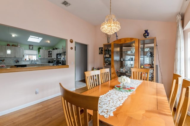 dining room with vaulted ceiling with skylight, a notable chandelier, wood finished floors, visible vents, and baseboards