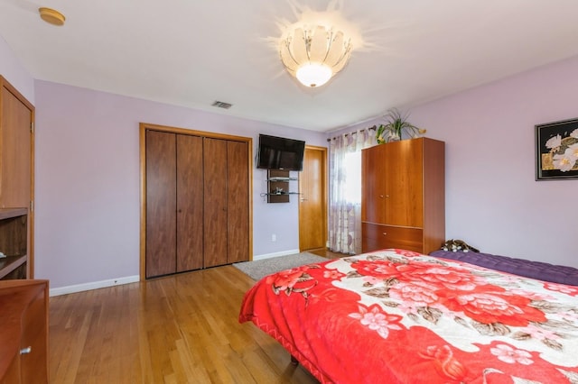 bedroom with light wood-type flooring, a closet, visible vents, and baseboards