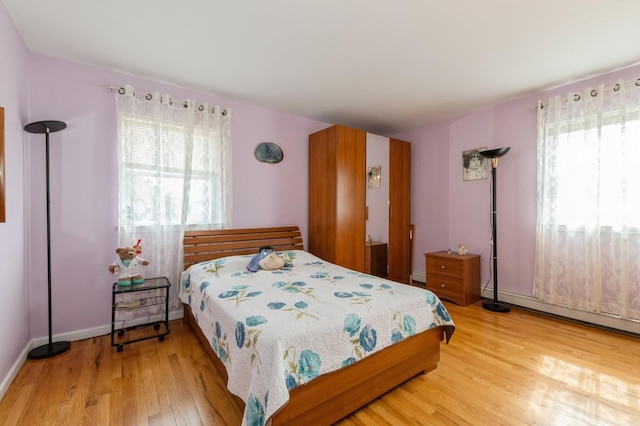 bedroom with a baseboard radiator, a baseboard heating unit, light wood-style flooring, and baseboards