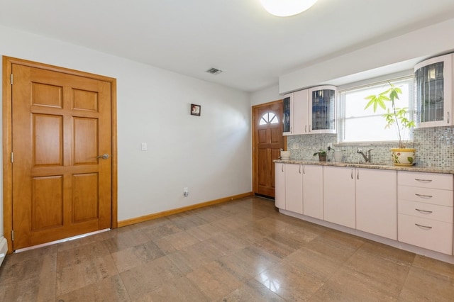 kitchen with glass insert cabinets, a sink, light stone counters, and backsplash