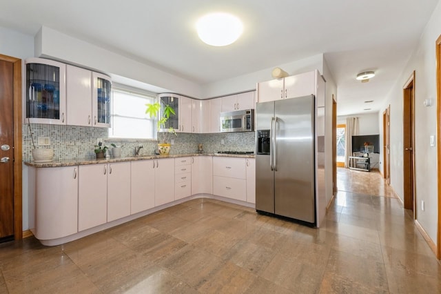 kitchen featuring light stone counters, stainless steel appliances, a sink, white cabinets, and backsplash