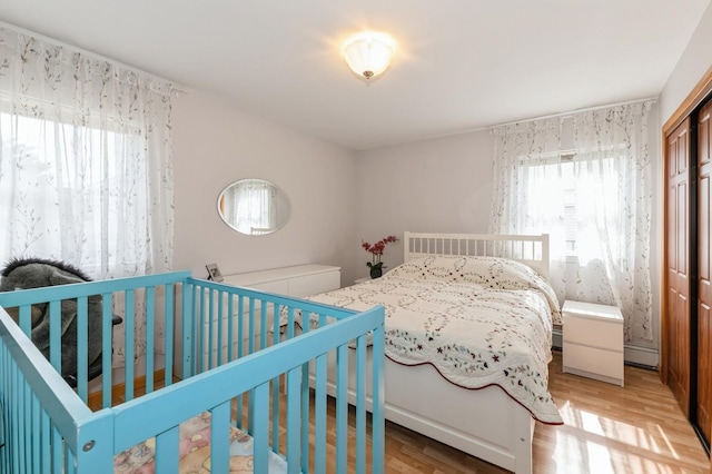 bedroom featuring light wood-style floors, a baseboard heating unit, and a closet