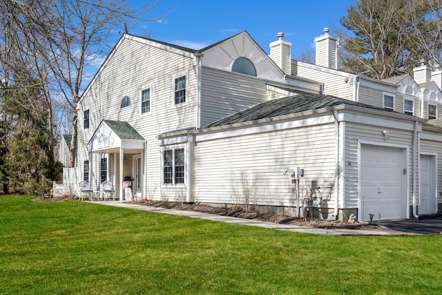 rear view of house featuring a yard, a garage, and a shingled roof