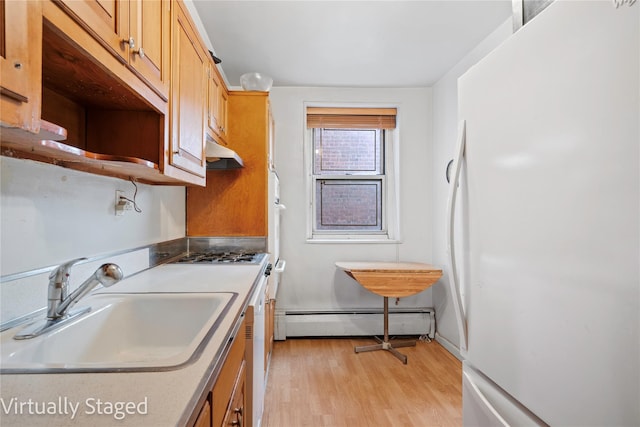 kitchen with a baseboard radiator, freestanding refrigerator, a sink, under cabinet range hood, and light wood-type flooring