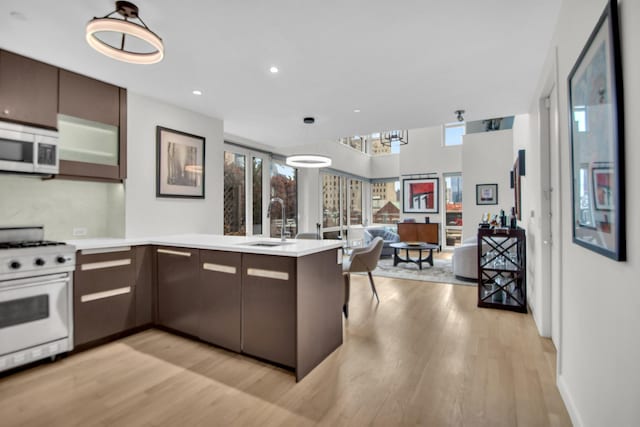 kitchen with white appliances, open floor plan, a peninsula, light countertops, and a sink