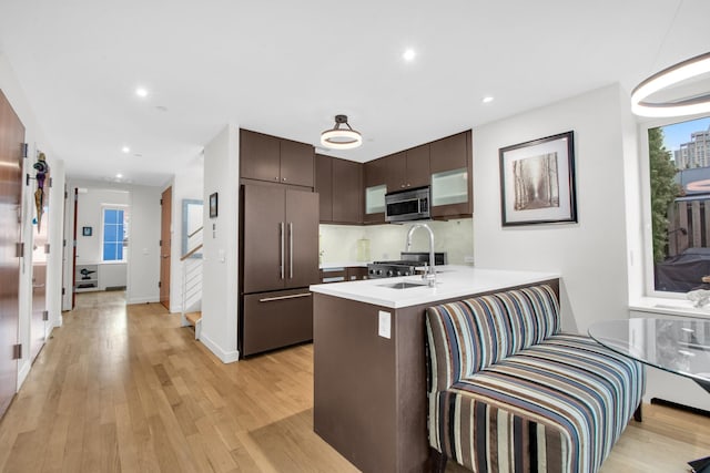 kitchen with light wood-style flooring, a peninsula, dark brown cabinets, appliances with stainless steel finishes, and light countertops