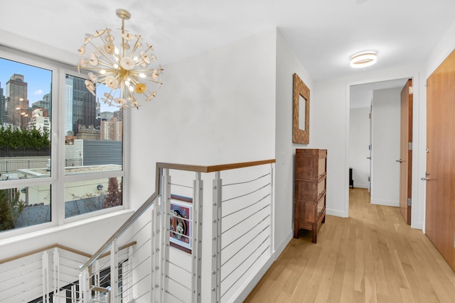 corridor featuring baseboards, a city view, an upstairs landing, light wood-type flooring, and a notable chandelier