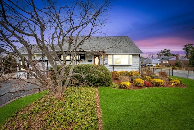 view of front of home with roof with shingles, a yard, and fence