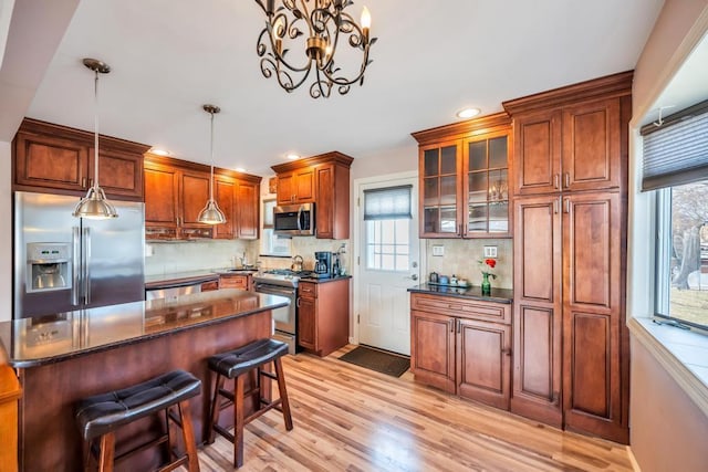 kitchen with light wood-style flooring, decorative light fixtures, tasteful backsplash, appliances with stainless steel finishes, and glass insert cabinets