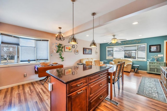 kitchen with dark countertops, baseboards, open floor plan, light wood-style flooring, and hanging light fixtures