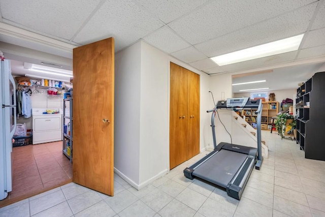 exercise area featuring tile patterned flooring, a drop ceiling, and washer / clothes dryer