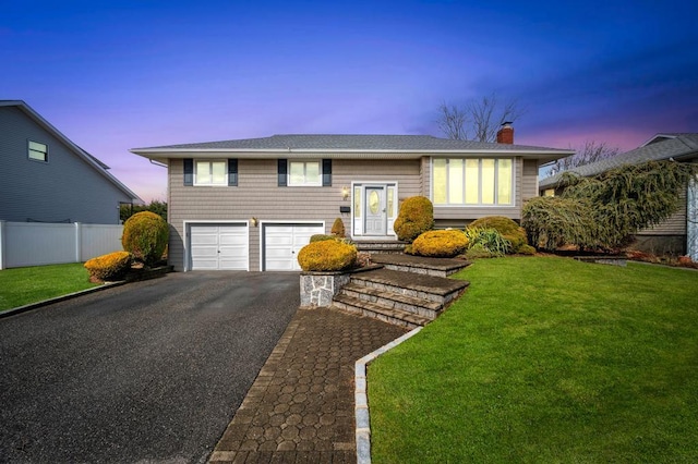 split foyer home featuring fence, a chimney, a front lawn, a garage, and aphalt driveway