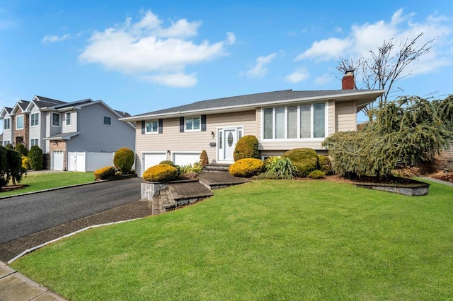 split foyer home with a front yard, fence, an attached garage, a chimney, and aphalt driveway