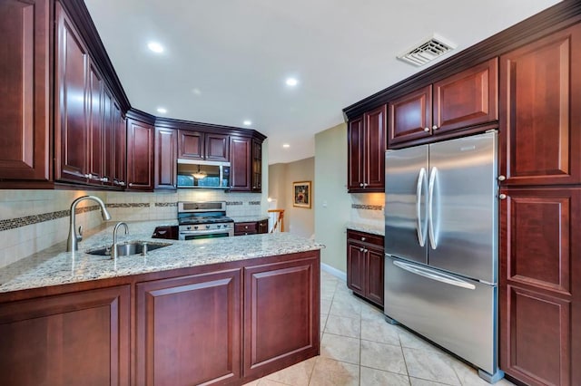 kitchen featuring light stone counters, visible vents, a sink, appliances with stainless steel finishes, and reddish brown cabinets