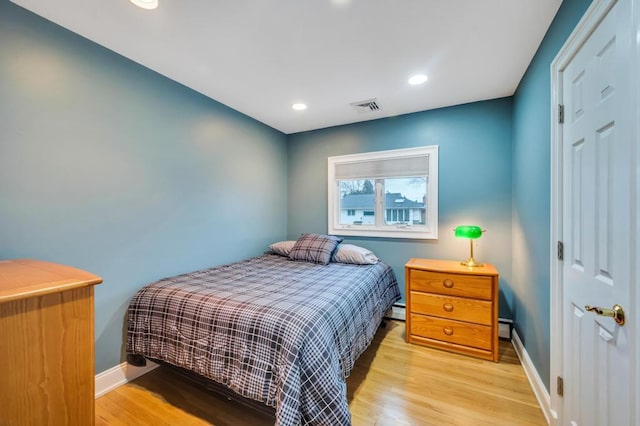 bedroom featuring a baseboard heating unit, baseboards, visible vents, and light wood finished floors