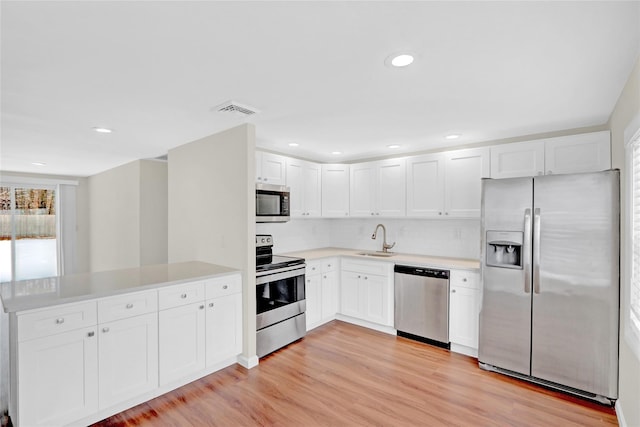 kitchen featuring a peninsula, a sink, stainless steel appliances, light countertops, and light wood-style floors