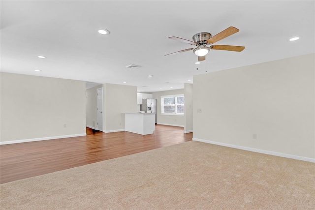 unfurnished living room featuring a ceiling fan, baseboards, light wood-style flooring, recessed lighting, and light carpet