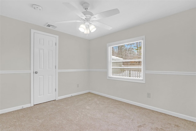 carpeted spare room with visible vents, baseboards, and a ceiling fan